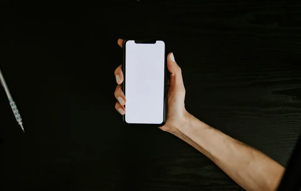 Mano sosteniendo un celular con la pantalla en blanco, sobre un fondo oscuro