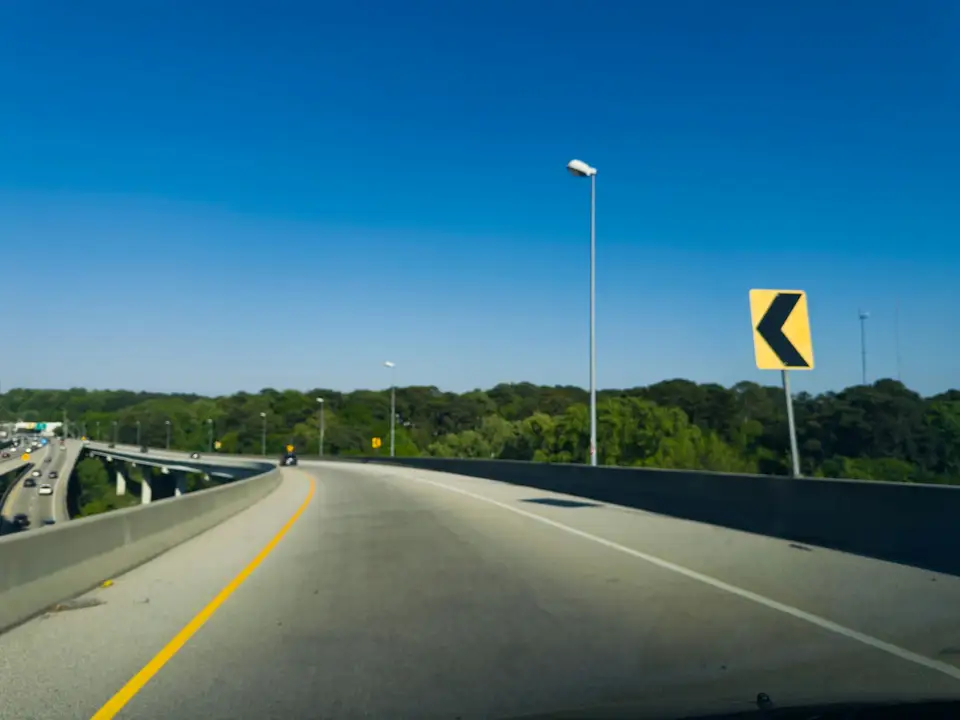Carretera que describe una curva, con una señal amarilla de curva al costado y el cielo despejado