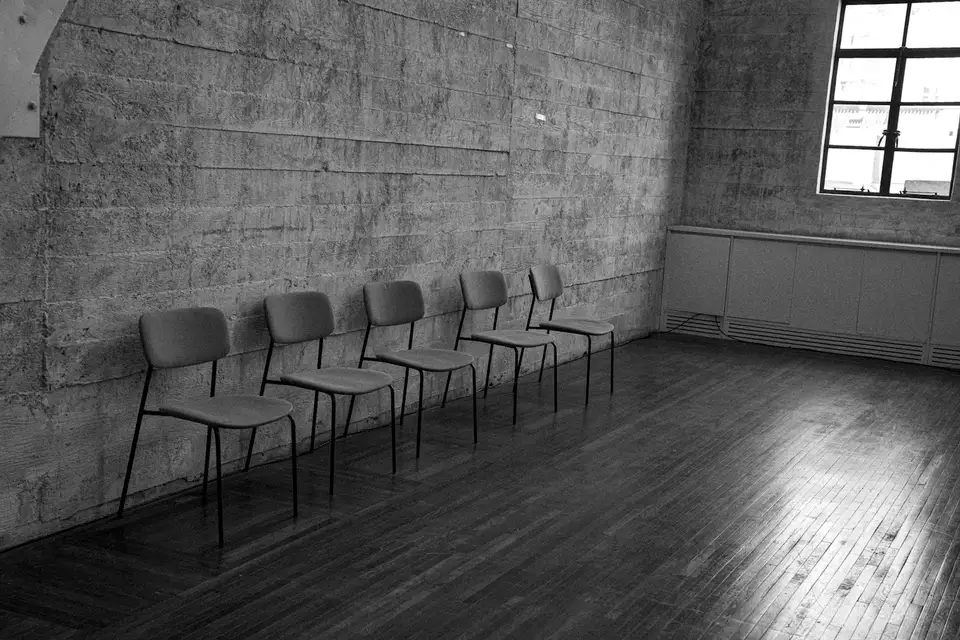 Fila de sillas vacías contra una pared de hormigón, en blanco y negro
